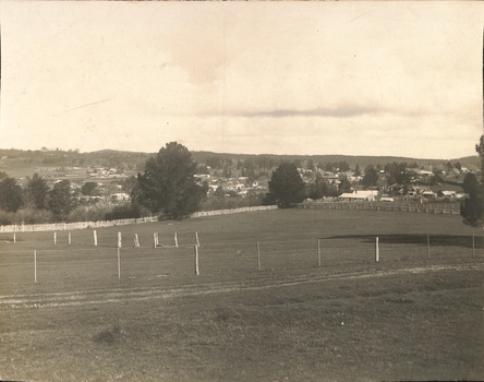 Distant view of township across open fields, trees line mid distance, hills beyond.