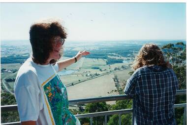 View from top of tower on Mount Buninyong across plain, fields disappearing into haze.  Lady on left gesturing.