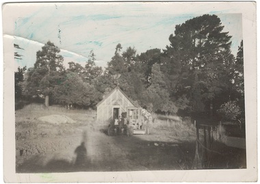 Monochrome photo, wooden lattice fernery in clearing, surrounded by established trees.