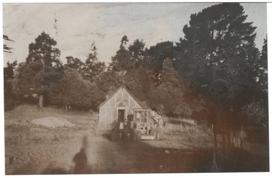 Monochrome photo, wooden lattice fernery in clearing, surrounded by established trees.