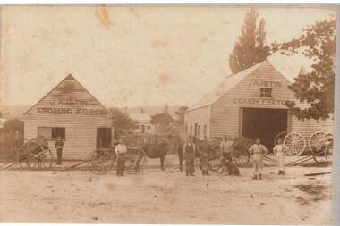 Two wooden industrial buildings, carts and wagons in front, horse and seven men most in shirt sleeves and aprons, one in suit, and a dog.