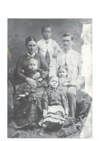 Family portrait in Victorian  clothes, husband seated right with toddler daughter on lap, wife seated left with younger son on lap,  older daughter seated in front and eldest son standing behind. 