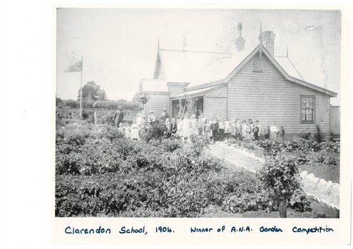 Wooden school building, single story, children and teachers lined up outside, well tended garden