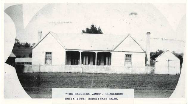 Whitewashed wooden building, gabled single window wing each side, with 3 bay recessed veranda between, chimneys either end, picket fence, shed on right.