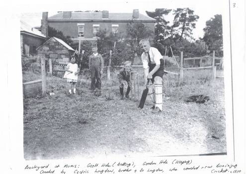 Boys and girl playing cricket in rough yard behind two-story house.