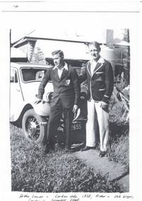 Two young men standin in front of Marris car, both wearing blazers, side of house in background.