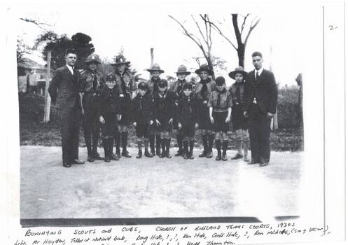 Boy scouts in uniform, lined up, Boy cubs in front, man in suit each end, bare trees behind.