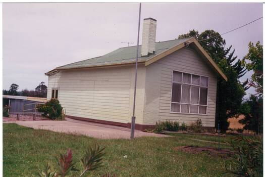 A single story building of the former Yendon Primary School converted to a private home painted cream with new wooden doors visible to the rear of the building