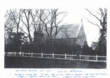 Side view of bluestone church through bare trees, high peaked slate roof, low square bell tower, 