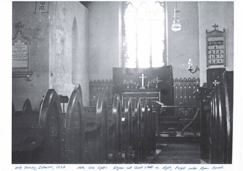 Interior of church, down aisle to altar, showing pews, stained glass window, gas lights.