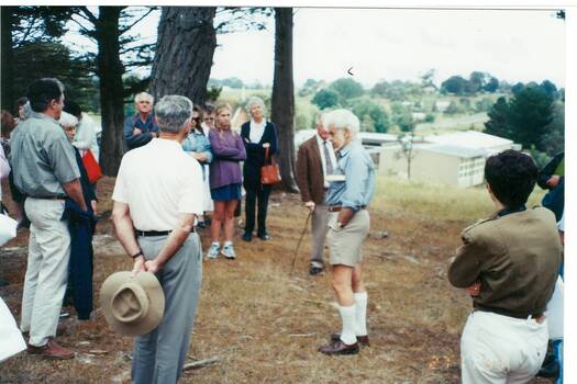 Group of people standing on hill side in front of cypress trees, modern school buildings below.