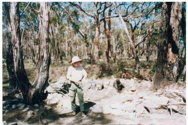 Woman on creek bank in bush, wearing t-shirt, cargo pants and solar topee.