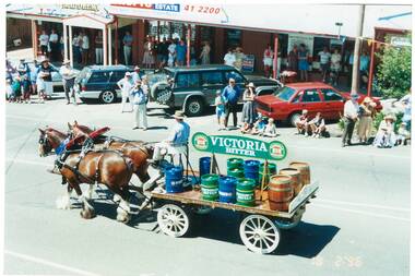 Pair of Clydesdale Horses pulling dray with beer barrels along street, people watching from roadside and under shop verandahs.