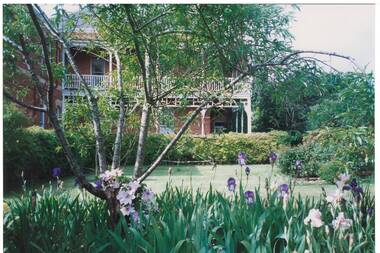 View of the side of Mount Boninyong Homestead showing garden bed of Irises, tree, hedging and lawn