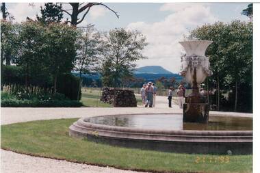 View of the garden and fountain at Larundel, a group of visitors gather on the driveway and Mount Buninyong is visible on the horizon