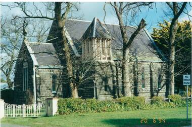 Side view, bluestone church through bare trees, slate roof, square bell tower.