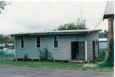 Small, plain weatherboard building, plain windows, wide, open doorway, flat roof.