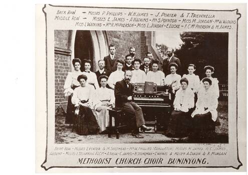 Mixed group of adults around portable church organ, in garden in front of church.