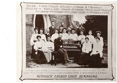 Mixed group of adults around portable church organ, in garden in front of church.
