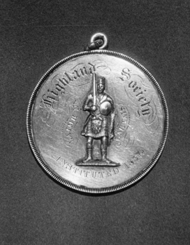 Close up of Highland Society medal showing a sword bearing raised warrior in full Highland dress and the words "Highland Society" Instituted 1857