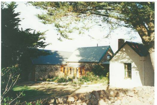 Low stone buildings, iron roofs, lawn in front, trees surrounding.