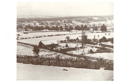 Winter landscape scene showing buildings, fences, and trees