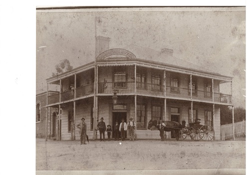 Two story corner hotel, wrap-around verandahs both floors, people around central door, horse and cart to right.