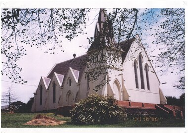 Colour photograph of Buninyong Uniting Church showing the Northern and Western facades of the building framed by the leaves and  branches of the trees in the grounds.