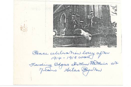 Three men in uniform standing in lorry tray in front of church.