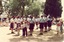 Children  watching pipe band in clearing in park, tall trees behind.