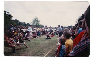 Tug of War, showing both teams, crowds of people either side, treetops behind.