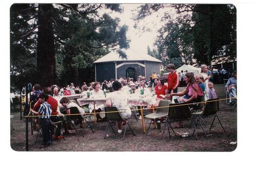 Crowd seated at lunch in park, rotunda behind, surrounded by trees.