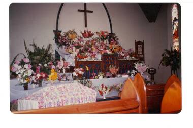 Floral display on altar in church, cross hanging on wall behind.