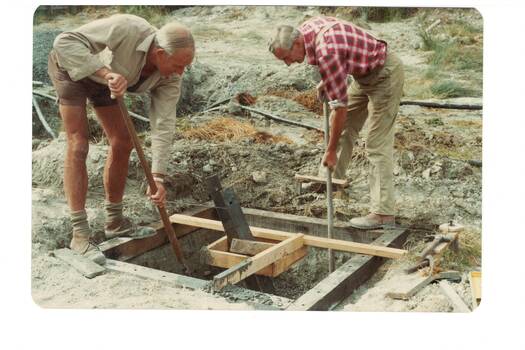 two  men in shirtsleeves digging out foundation hole in wooden frame