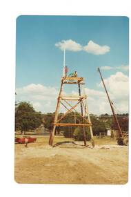 Partially complete log poppet head, small mobile crane beside it at full extension. In park, soil freshly graded.