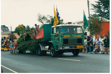 Flat bed truck on road, boy scouts on truck bed, people lining street.