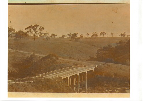 Photo of concrete bridge spanning gully, rolling landscape with scattered trees. 