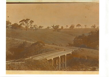 Photo of concrete bridge spanning gully, rolling landscape with scattered trees. 
