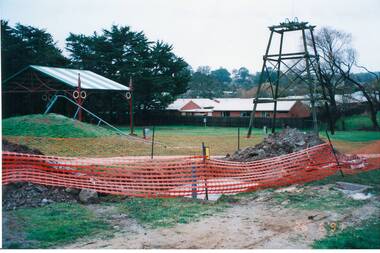 Construction area in park, screened off, poppet head and awning in background.