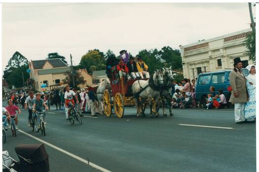 Horse-drawn cart on street next to cyclists, people lining the street.