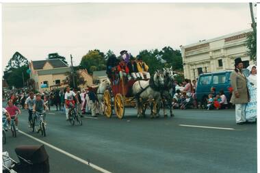 Horse-drawn cart on street next to cyclists, people lining the street.