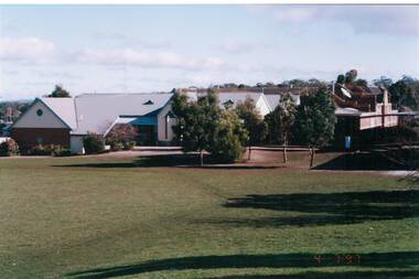 Looking across oval to school buildings, trees planted centre.