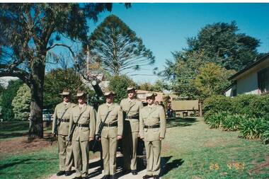Five army serviceman at attention in park, barrel of cannon behind them.
