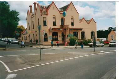 Photo across intersection of two-story hotel, rendered brick, high gables and ornate chimneys.