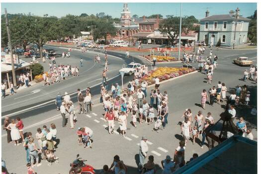 View down on parade going through intersection, people lined up watching.
