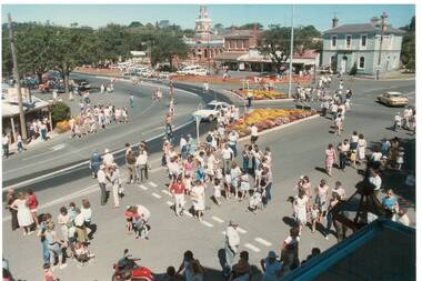 View down on parade going through intersection, people lined up watching.