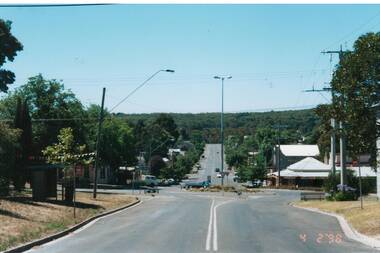 Photo looking downhill across intersection, Trees both sides, scattered buiuldings.