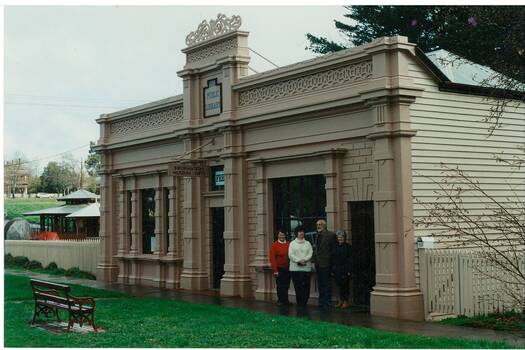 Old wooden single story building, ornate wooden facade, four people standing in front.