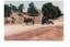 Two horse-drawn carts on dirt road, school in distance.