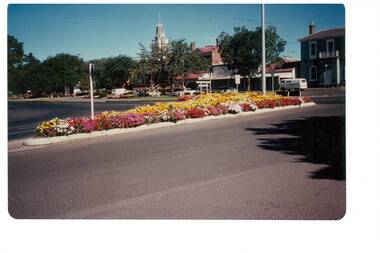 Colour photograph of the intersection of Warrenheip and Learmonth Streets showing the colourful planting of the traffic islands with the Town Hall, shops and the old National Bank in the background